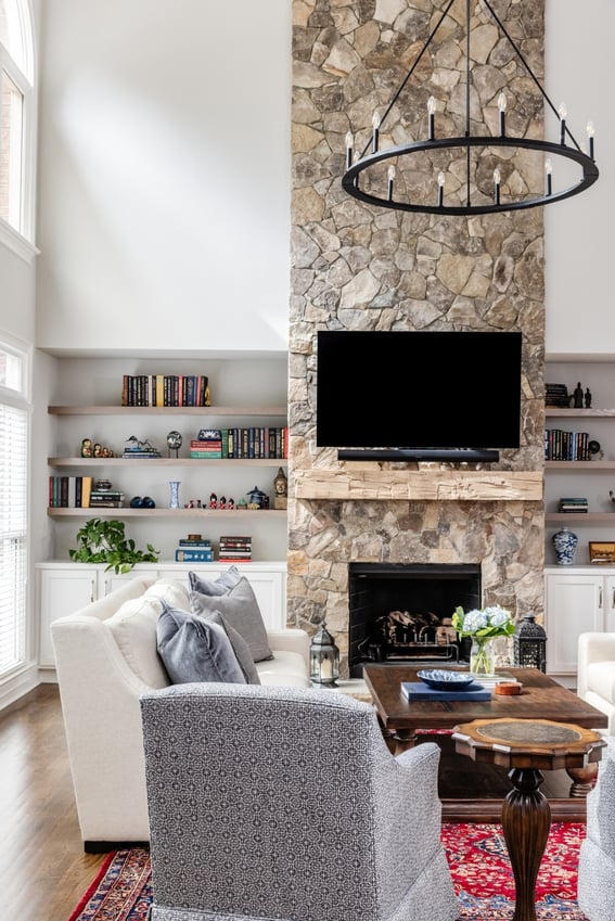 Remodeled living room featuring a stone fireplace, a statement chandelier, and floor-to-ceiling windows by Simonini Homes in Charlotte, NC
