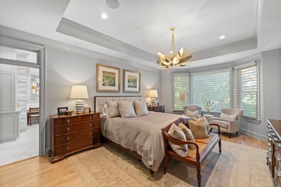 Luxurious primary bedroom with tray ceiling and modern chandelier from a renovation in Ballantyne, NC