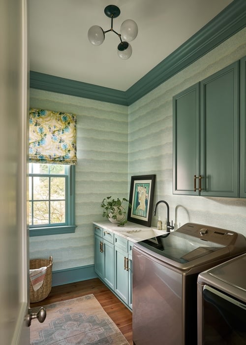 Elegant laundry room with patterned wallpaper and teal cabinetry in Charlotte custom home by Simonini Homes